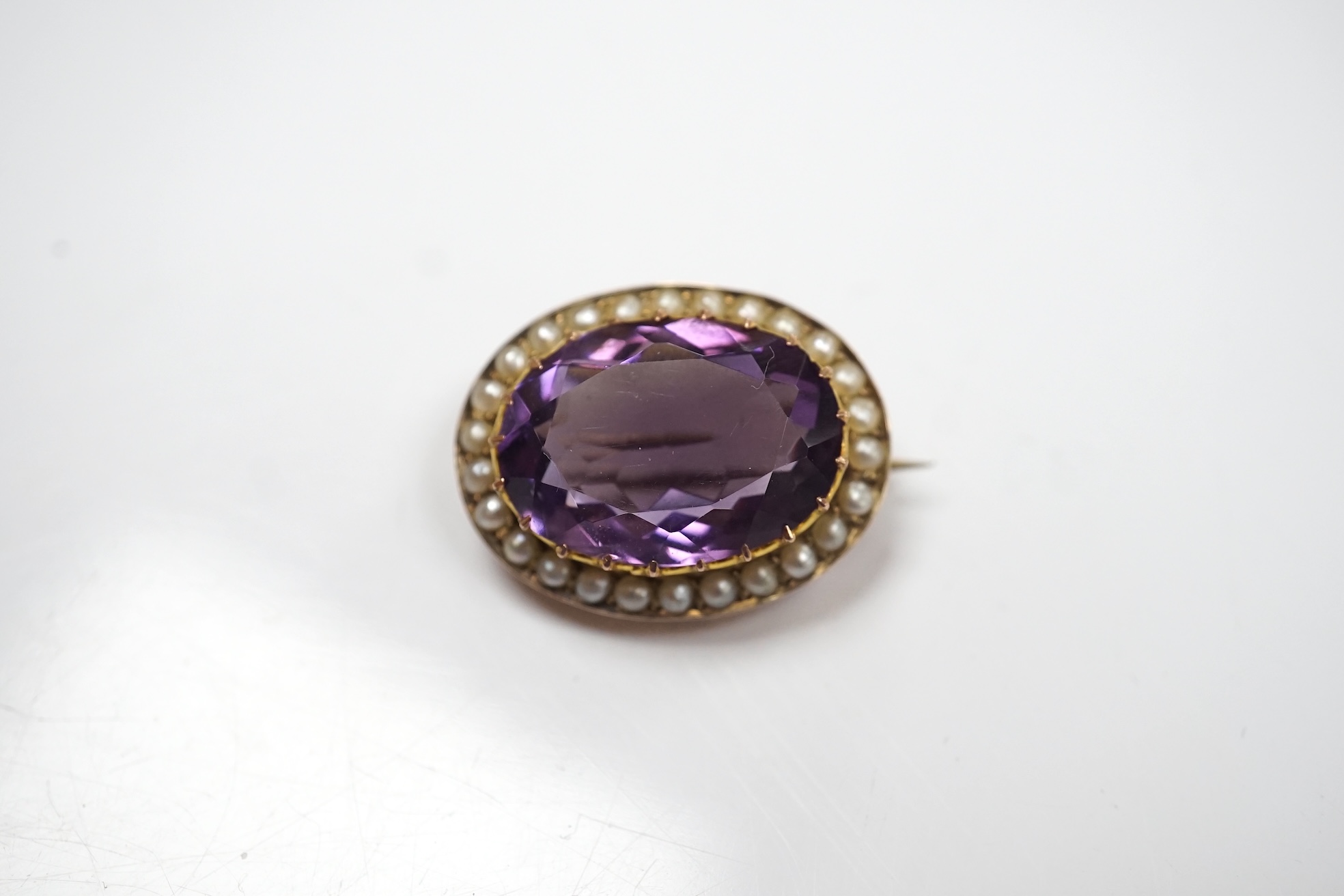 A mid 20th century 9ct and single stone oval cut amethyst set pendant brooch, with seed pearl border, 24mm, gross weight 4.8 grams. Condition - fair to good